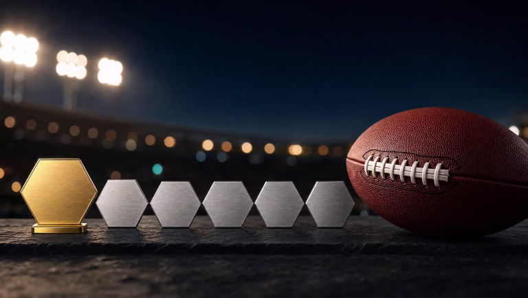A gold hexagon tile on a stand beside five silver tiles and a football under blurred stadium lights